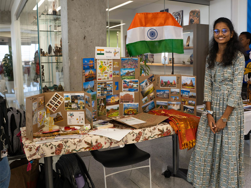 Student from India beside display table at International Week Showcase